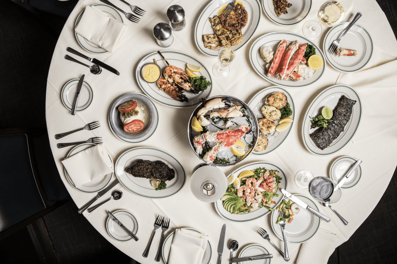 over head photo of a round table with a white table cloth, set for dinner with a variety of menu items in the middle of the table